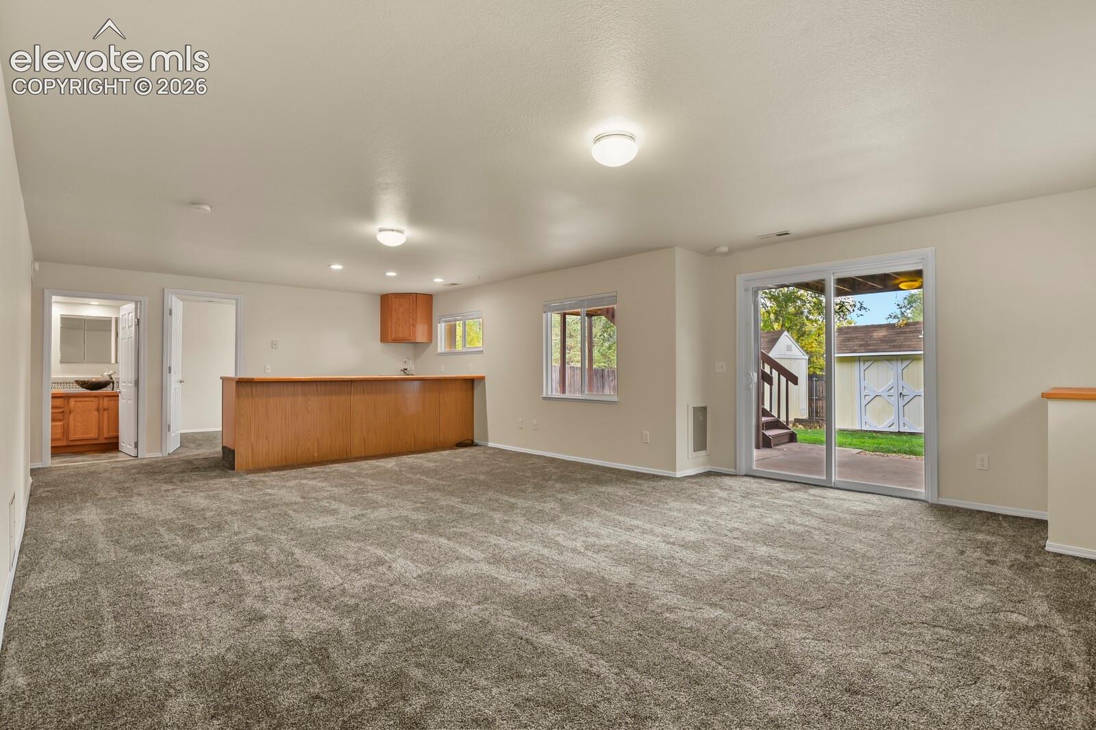 Spacious interior featuring neutral carpeting, a built-in wood-finish wet bar, and sliding glass doors with exterior access