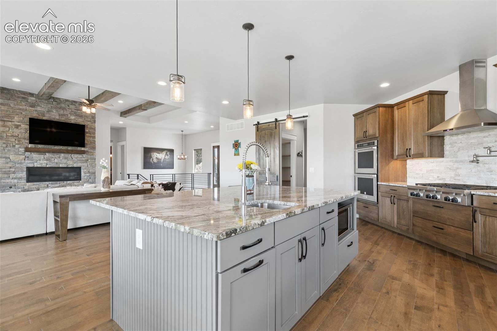 Gourmet kitchen with double ovens, a gas range, and a large central island featuring a stainless steel sink, microwave, and pendant lighting