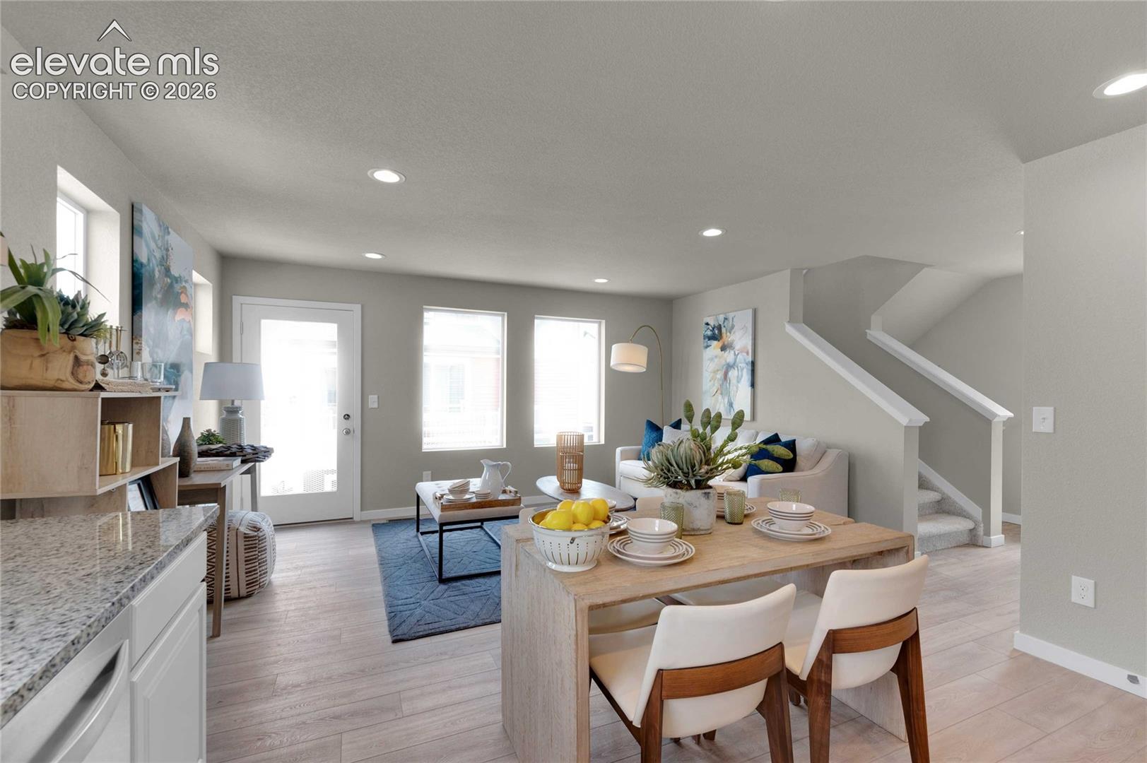 Open-concept living area with abundant natural light, recessed lighting, wood-finish flooring, and a staircase with white balusters
*photos of a model home*