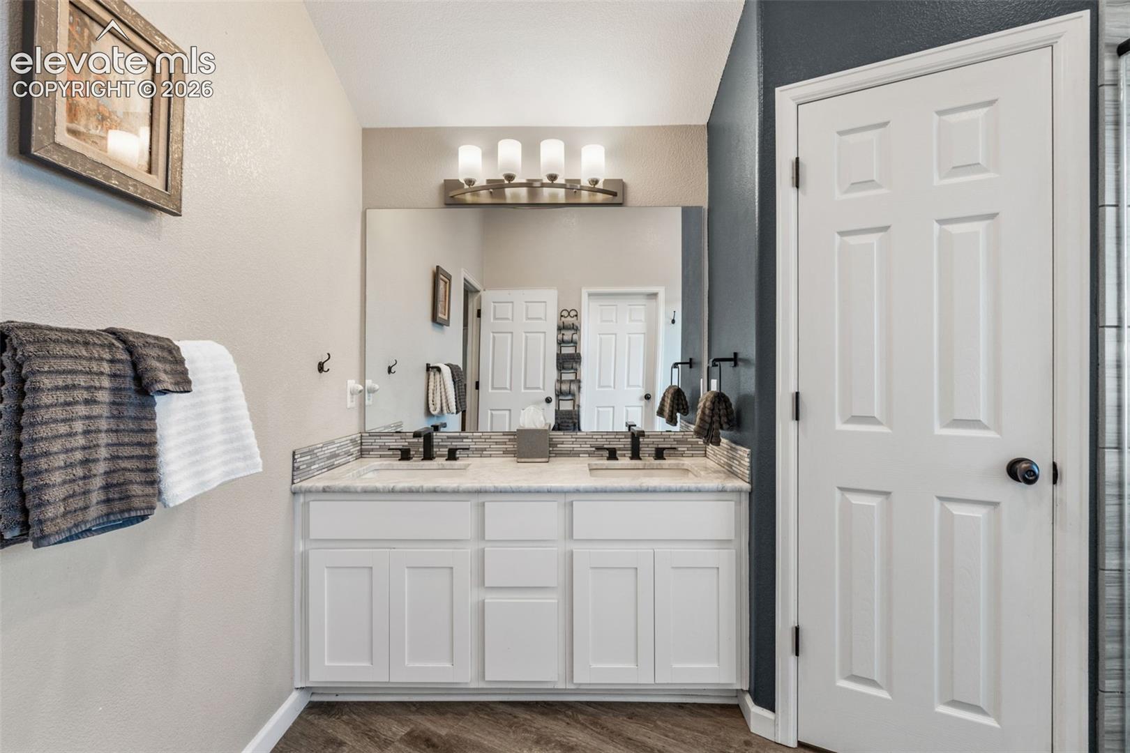 Dual-vanity cabinet with stone-finish countertop, undermount sinks, matte black fixtures, full-width mirror, and multi-light vanity fixture