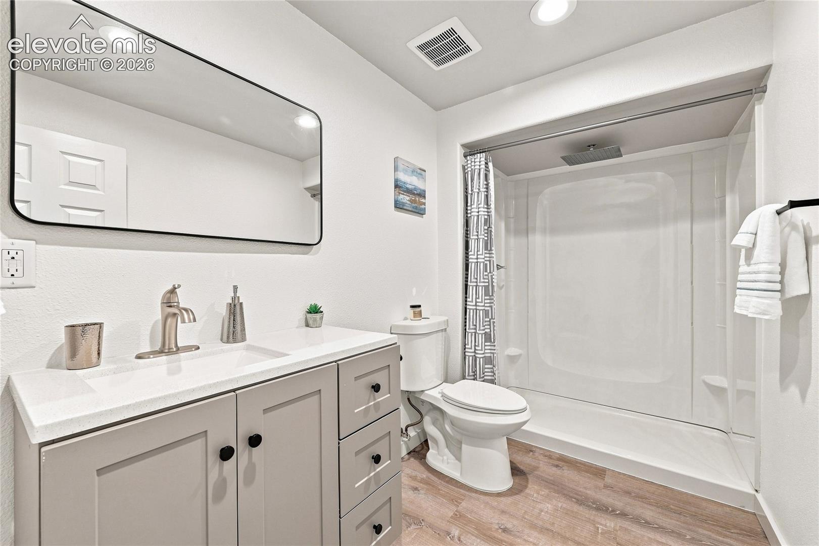 Vanity with a white countertop and integrated sink, brushed nickel faucet, large rectangular mirror, and wood-finish flooring