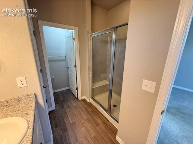 Wood-finish flooring leading to a glass-enclosed shower with a built-in bench, complemented by a vanity with a white countertop and integrated sink