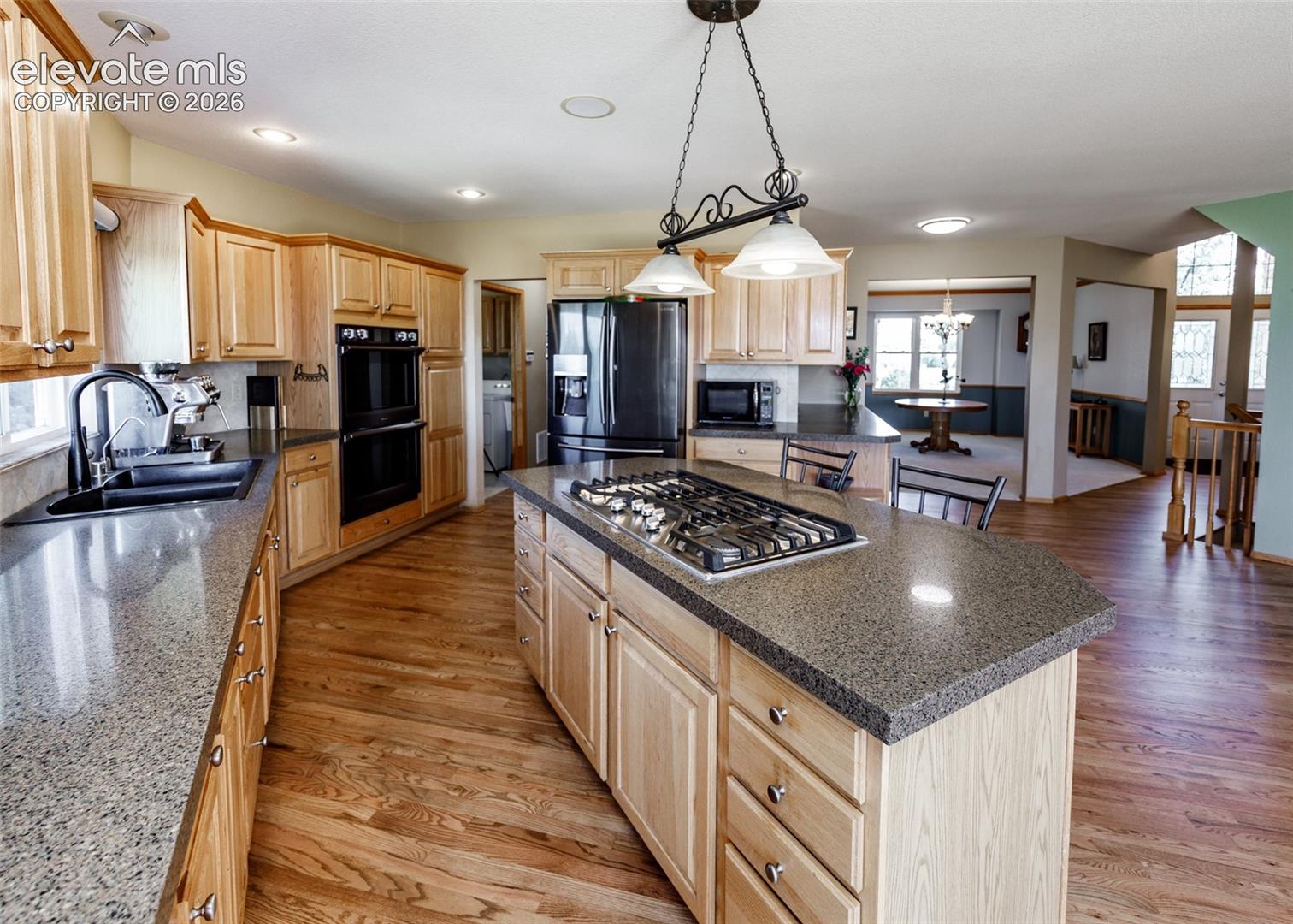 Kitchen featuring wood-finish flooring, light wood cabinetry, stone-finish countertops, a double oven, and a kitchen island with a gas cooktop