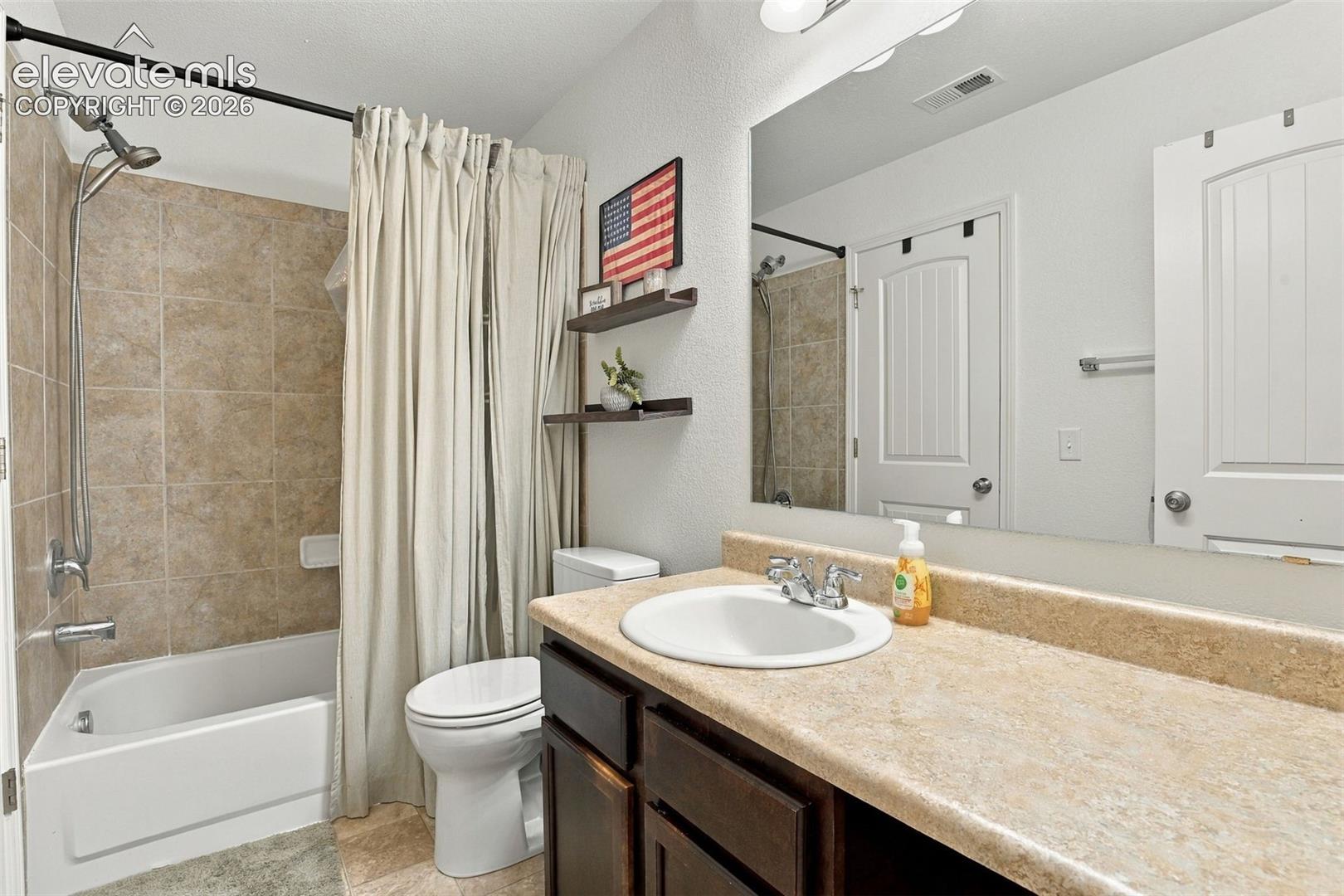 Vanity with an integrated sink, a large mirror, and a bathtub with tiled walls