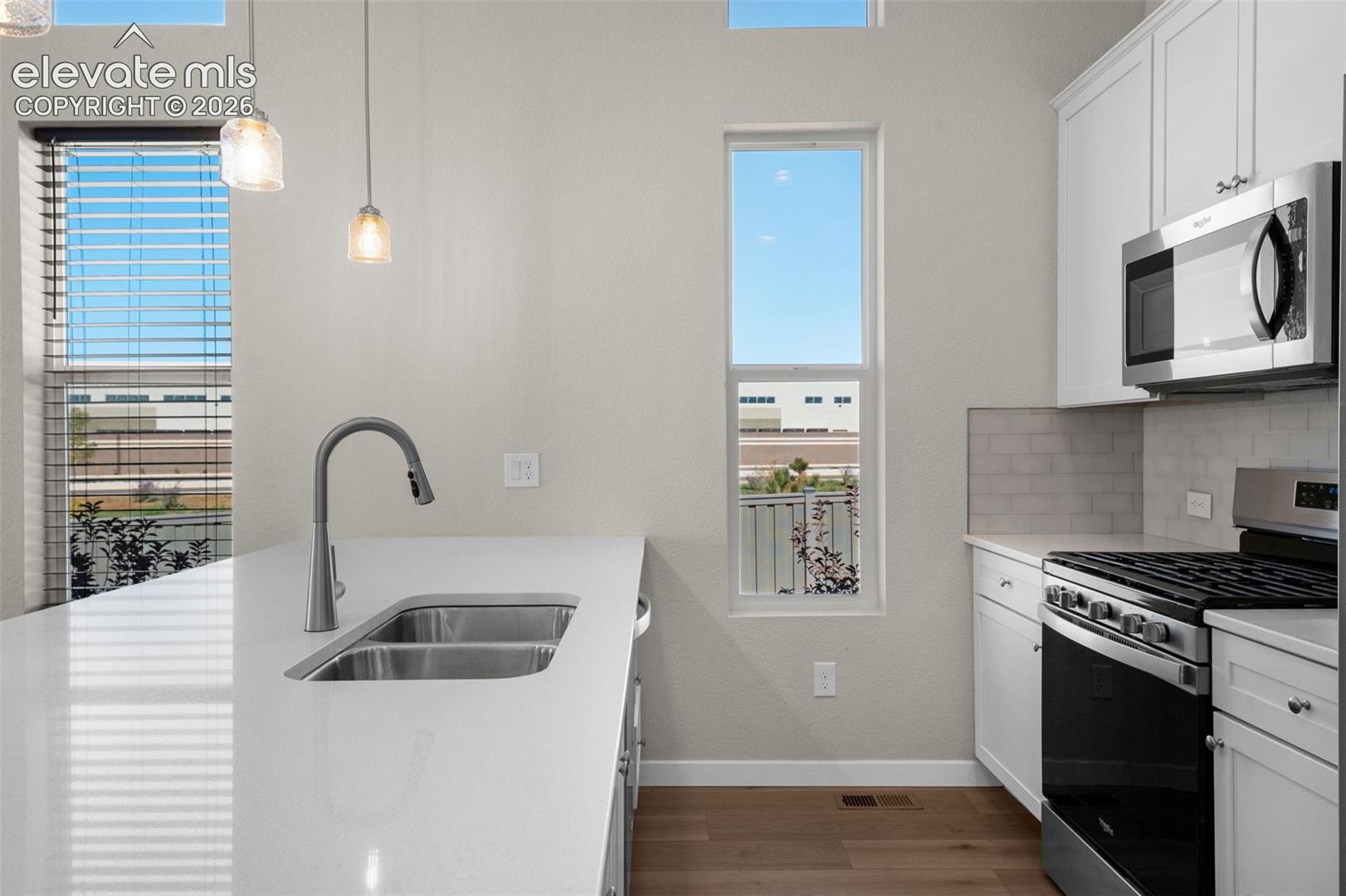 Kitchen featuring white cabinetry, quartz countertops, a dual-basin undermount sink with a gooseneck faucet, subway tile backsplash, and stainless steel appliances