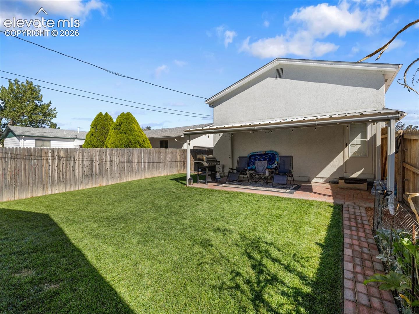 Expansive lawn area, private wood fencing, and a covered patio with brick paver flooring