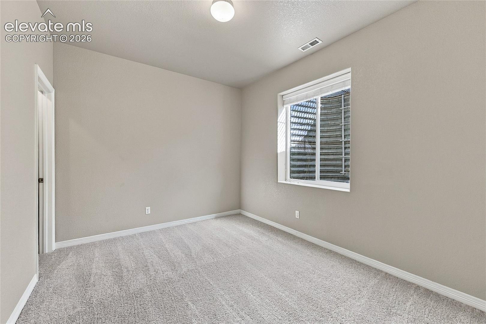 Neutral-toned interior room featuring wall-to-wall carpeting, a sliding window with integrated egress well, and a ceiling-mounted light fixture
