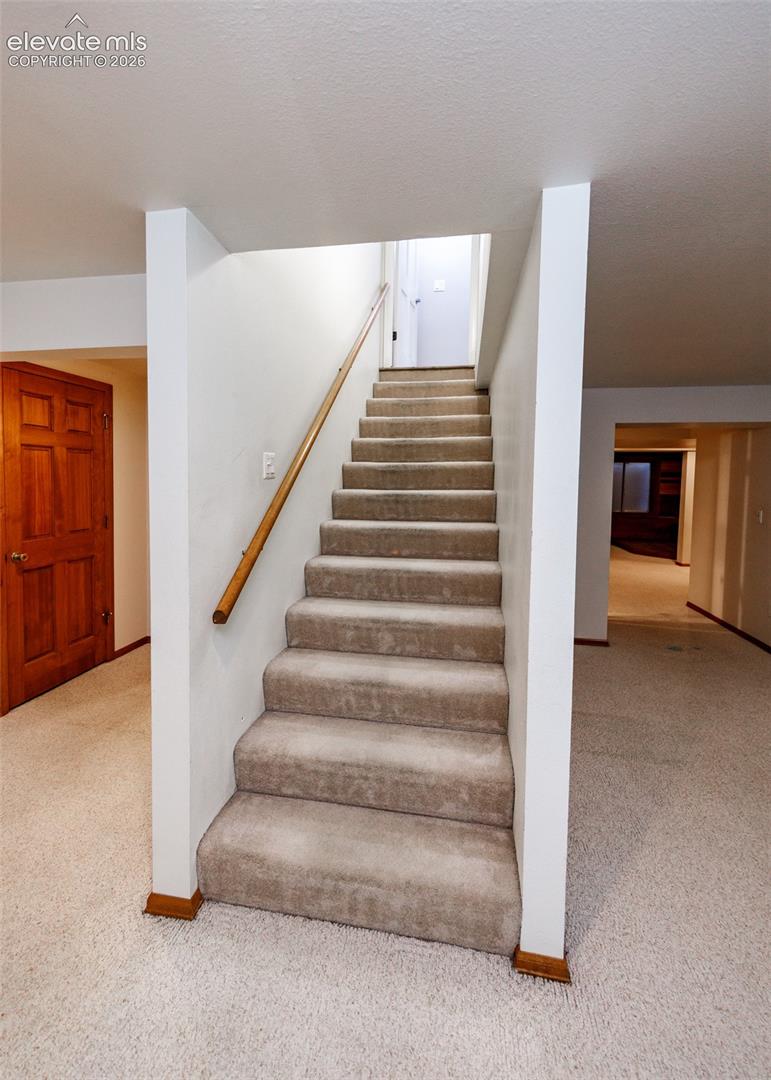 Carpeted staircase with a wood-finish handrail, surrounded by neutral wall tones and coordinating carpeted flooring