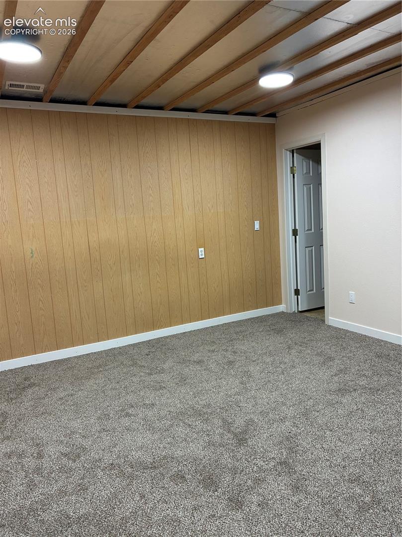 Room featuring exposed ceiling joists, wood-finish paneling, gray wall-to-wall carpeting, and flush-mount ceiling lighting