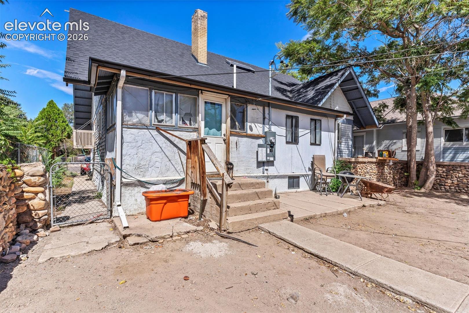 Rear exterior featuring a concrete patio, wood steps, and a chain-link fence