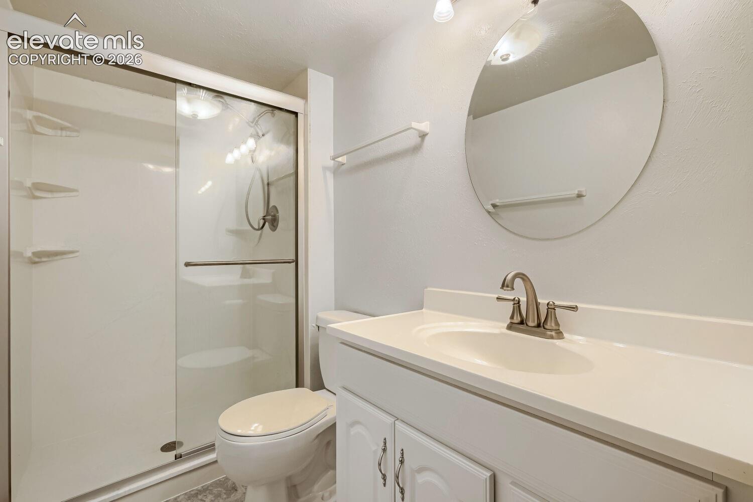 Shower with sliding glass enclosure, white vanity with integrated sink, brushed nickel faucet, and circular mirror