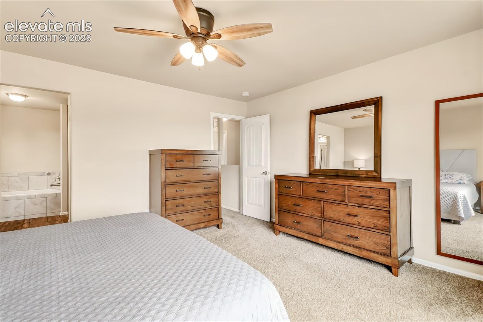 Neutral carpeting, multi-blade ceiling fan with integrated lighting, and a six-panel interior door