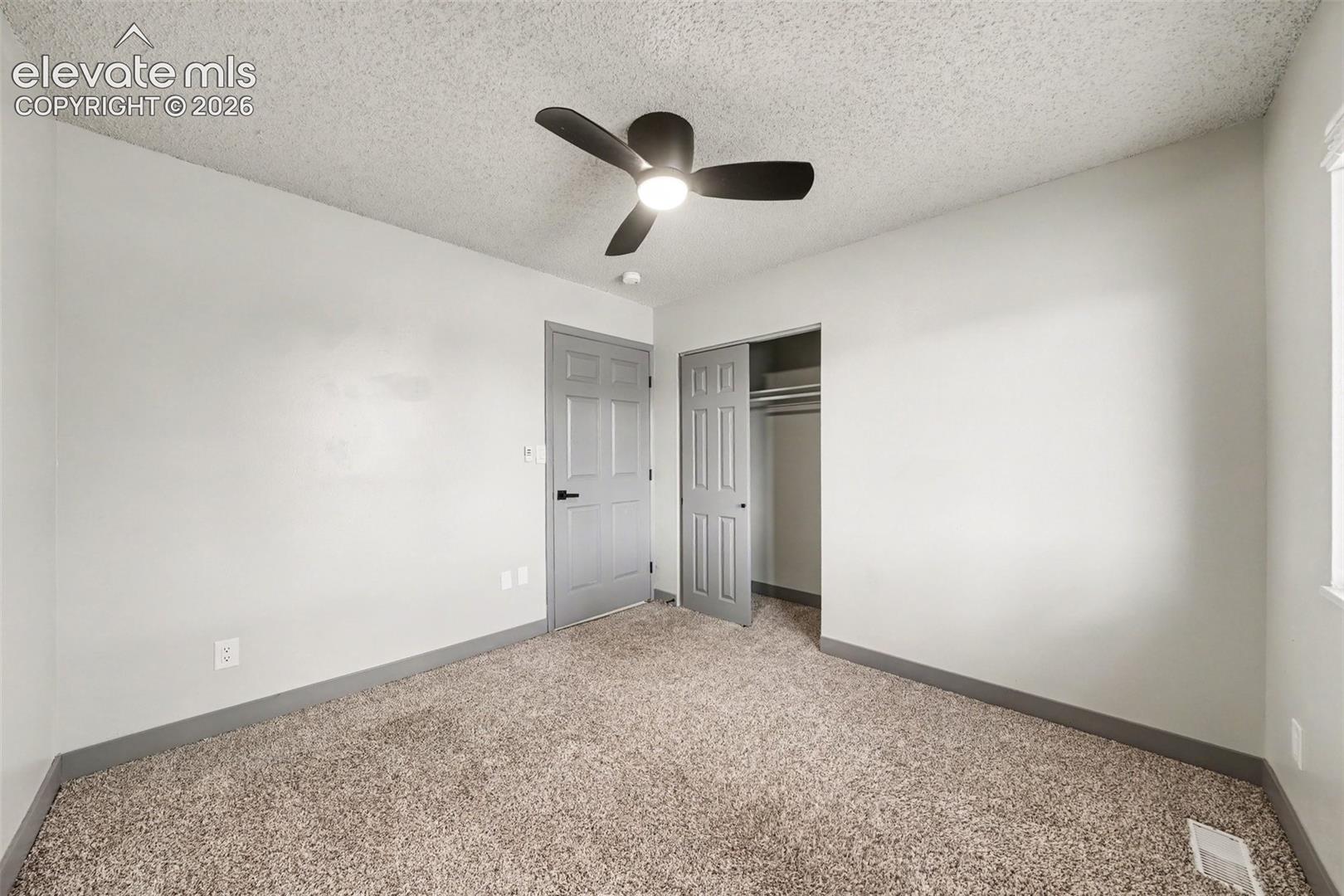 Neutral-toned interior featuring wall-to-wall carpeting, a matte black three-blade ceiling fan with integrated lighting, and a closet with a six-panel door