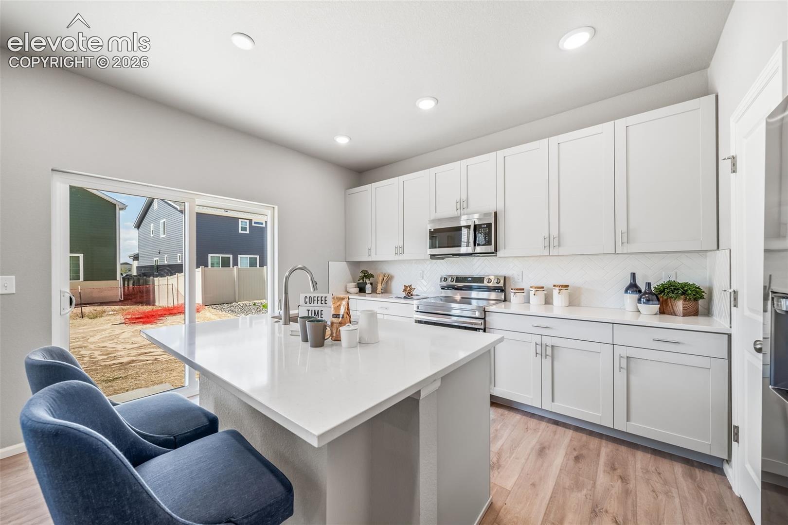 Kitchen featuring a center island with a sink, stainless steel appliances, white cabinetry, and wood-finish flooring
*photos of a model home*