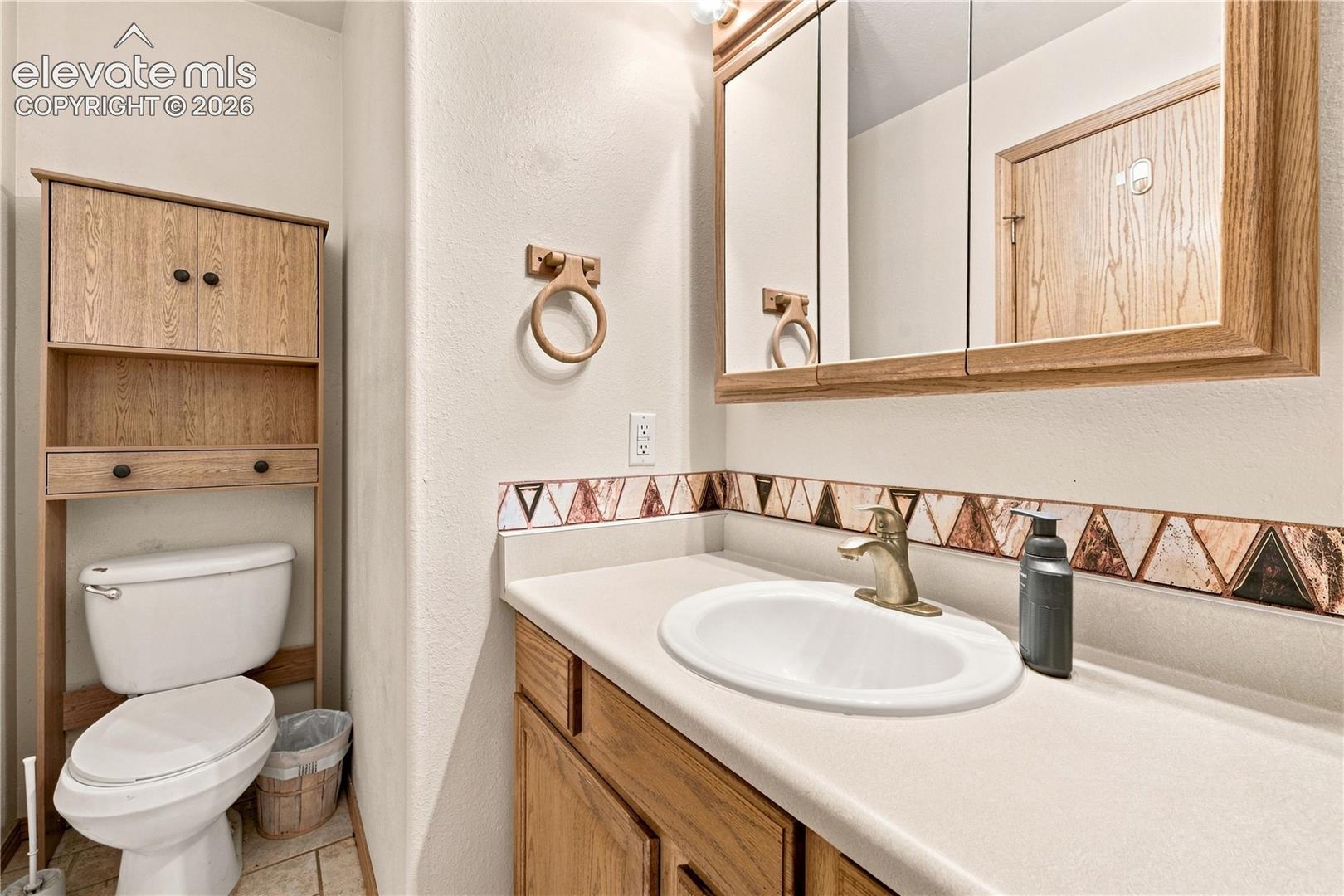 Vanity with an integrated sink, framed mirrored medicine cabinet, wood-finish cabinetry, and a geometric tile backsplash