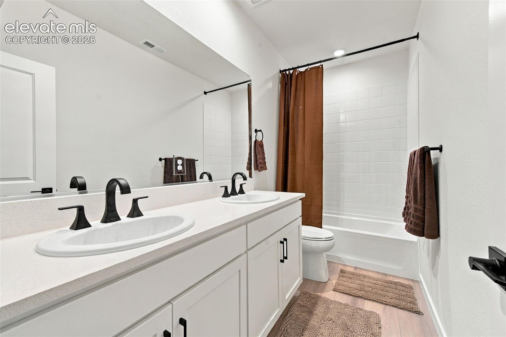Double vanity featuring white cabinetry, quartz-style countertops, integrated dual sinks, and matte black hardware with coordinating fixtures