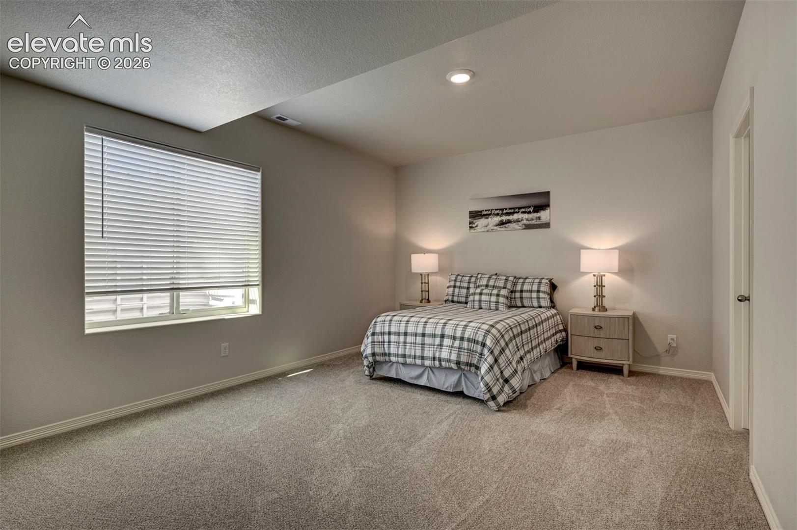 Spacious room featuring neutral carpeting, recessed ceiling lighting, a large window with horizontal blinds, and a white interior door