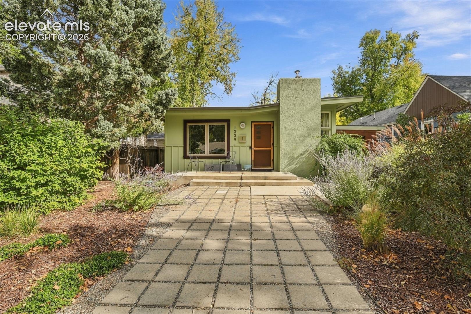 Mid-century exterior featuring vertical wood siding, a prominent concrete chimney, square concrete pavers, and a covered entryway