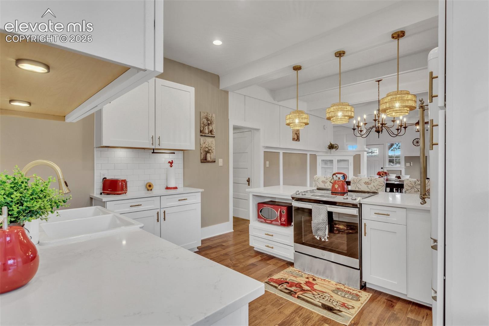 Kitchen featuring white cabinetry, quartz countertops, subway tile backsplash, stainless steel range, and wood-finish flooring