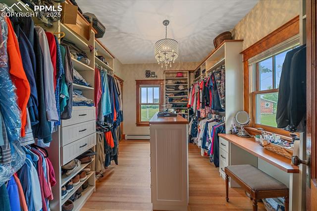 Spacious closet featuring light wood finished floors, a chandelier, and a baseboard heating unit