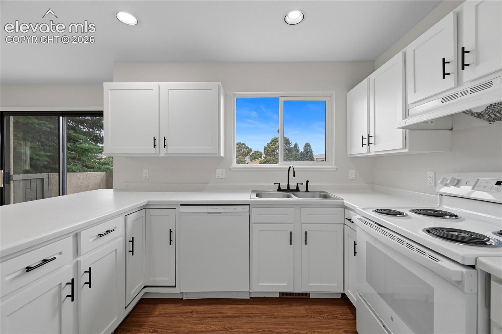 Kitchen featuring white cabinetry with matte black hardware, solid surface countertops, wood-finish flooring, recessed lighting, and a stainless steel dual-basin sink