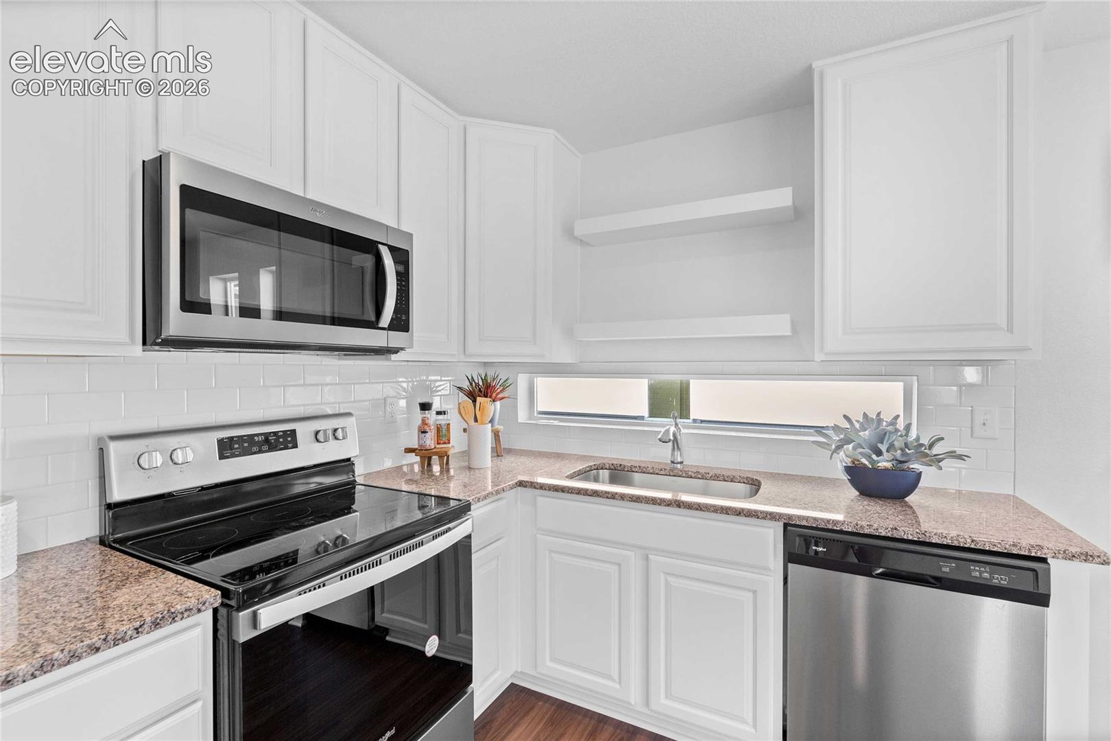 Kitchen featuring white cabinetry, granite-style countertops, stainless steel microwave, and white subway tile backsplash
*photos of a model home*