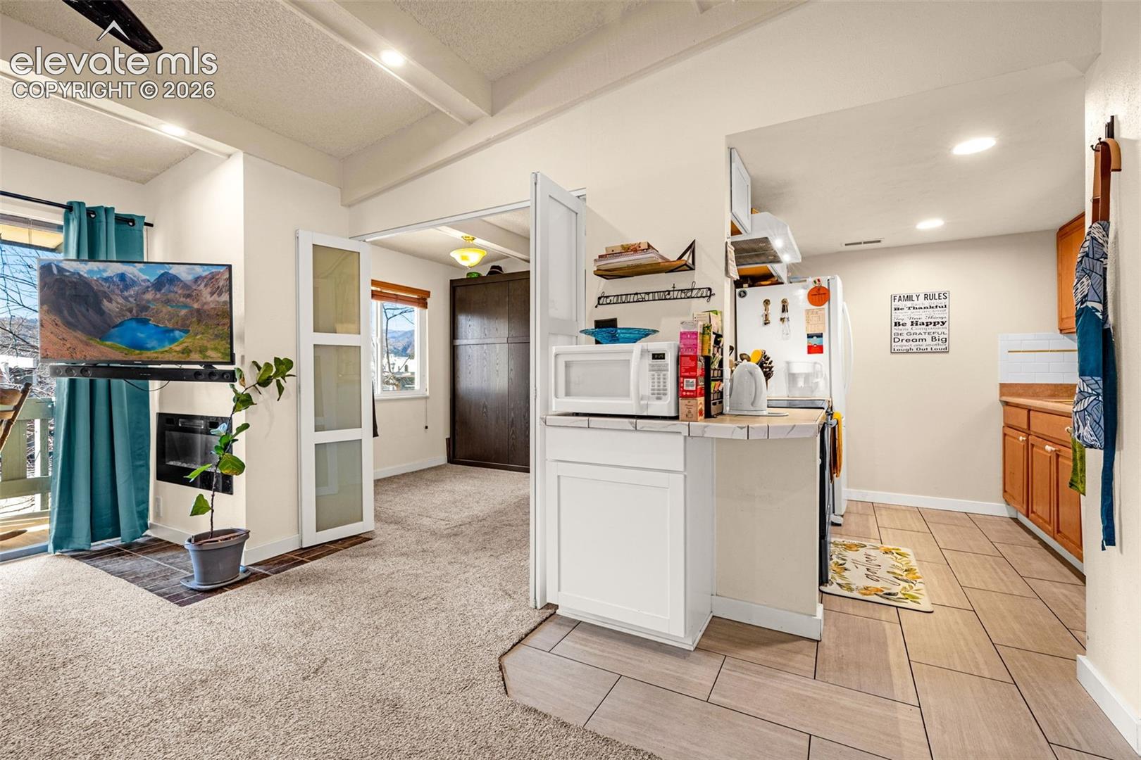 Tile flooring in kitchen, carpet flooring in living area, white kitchen cabinetry, wood-finish kitchen cabinetry, built-in oven