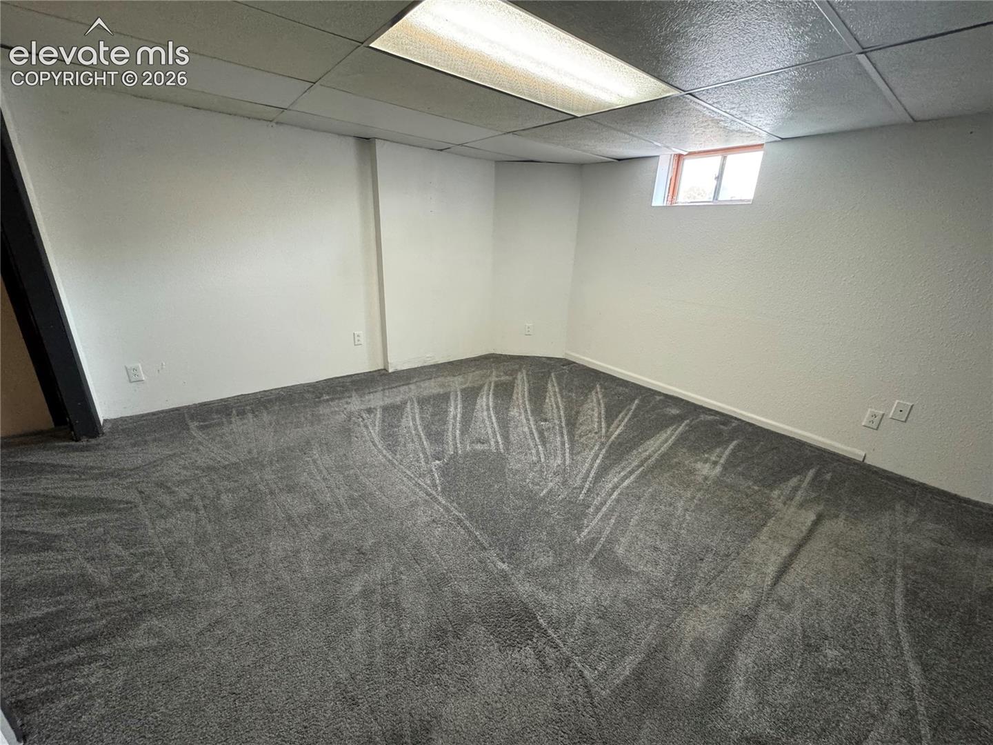 Finished room featuring wall-to-wall carpeting, white interior walls, a drop ceiling with recessed lighting, and a single pane window