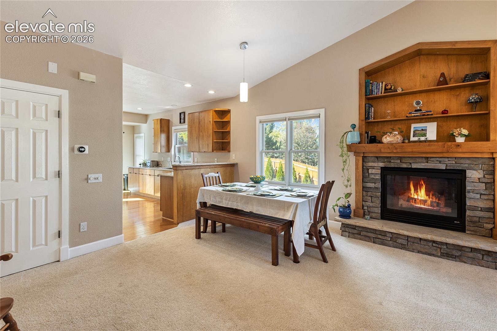 Vaulted ceilings, a stone-surround fireplace with a wood mantle, built-in shelving, a large window, and wood-finish flooring
