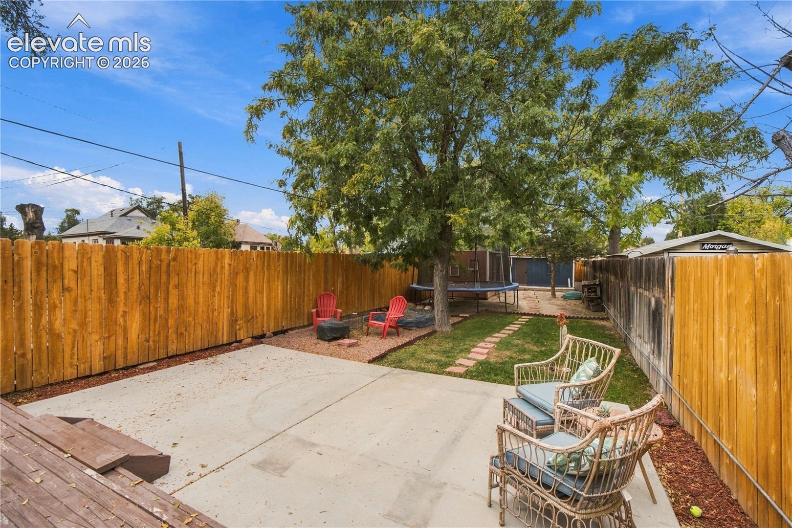 Backyard featuring a concrete patio, wood fencing, a grass lawn, stone-surfaced ground cover, and mature trees