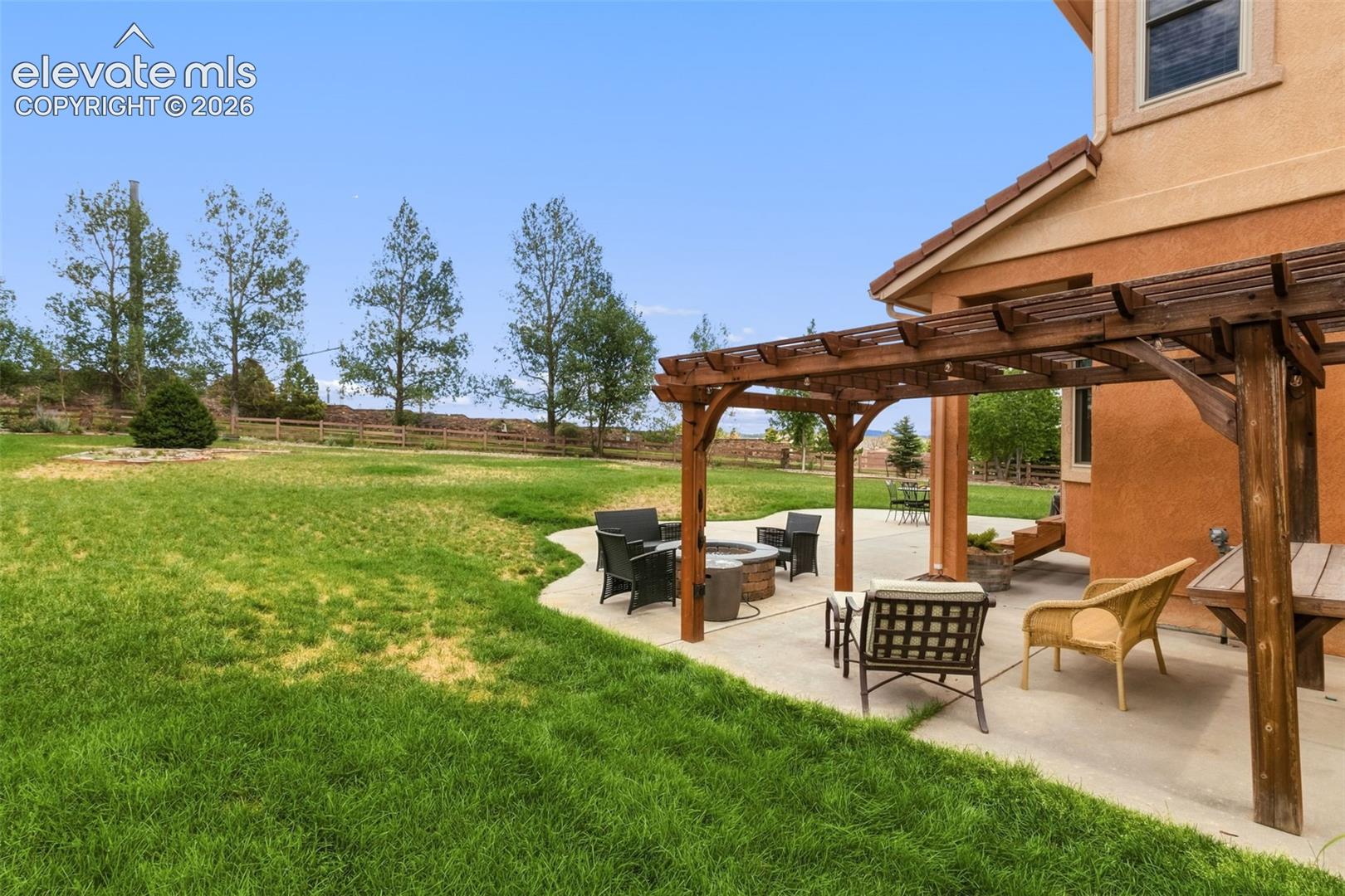 Spacious stucco exterior featuring a concrete patio with a wooden pergola, an integrated fire pit, and a sprawling grassy yard