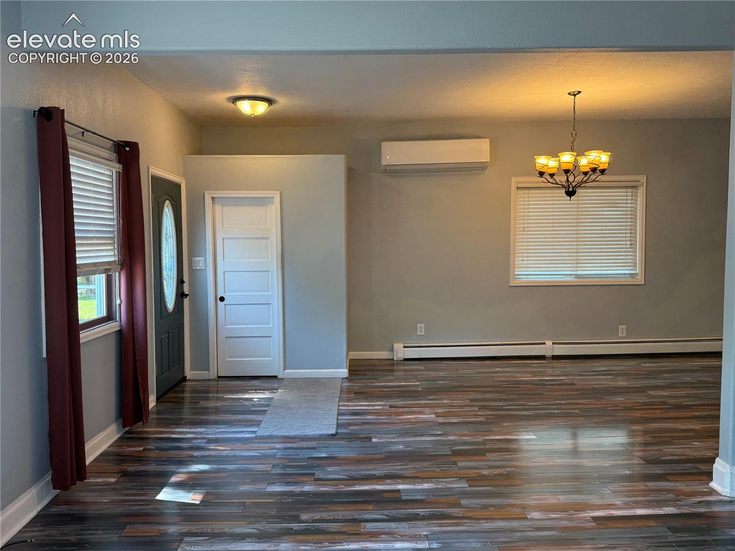 Multi-toned wood-finish flooring, wall-mounted ductless heating and cooling unit, multi-paneled interior door, and multi-light chandelier fixture
