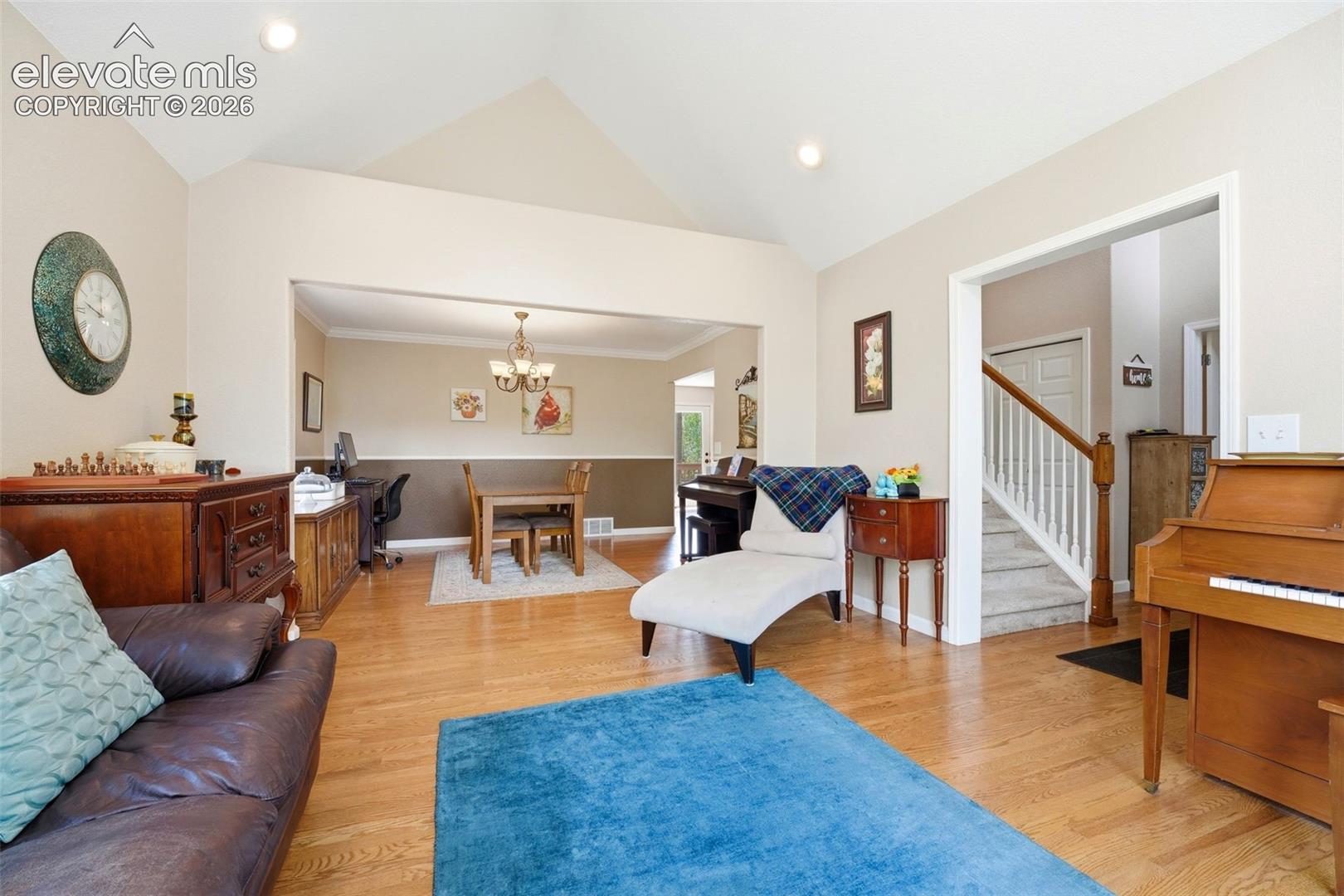 Vaulted ceiling living space featuring wood-finish flooring, recessed lighting, and an open entryway to a separate dining area with a chandelier