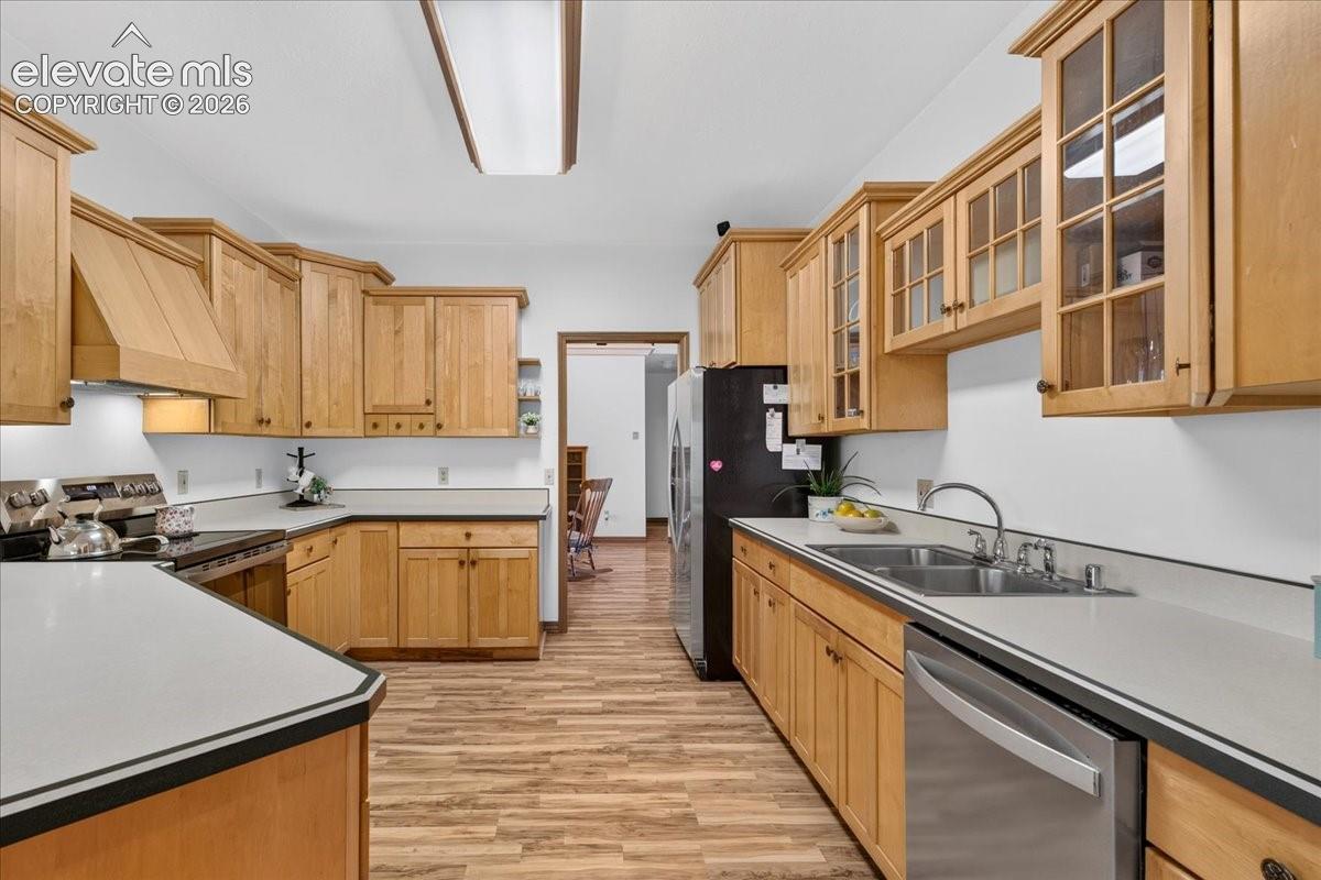 Kitchen featuring natural wood cabinetry, glass-front upper cabinets, solid surface countertops, a stainless steel double-basin sink, and wood-finish flooring