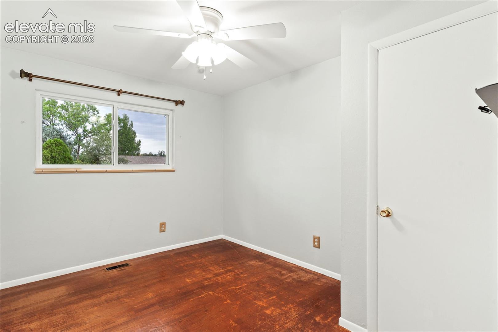 Window with natural scenery, ceiling fan, white paneled door, wood-finish flooring, and light wall paint
