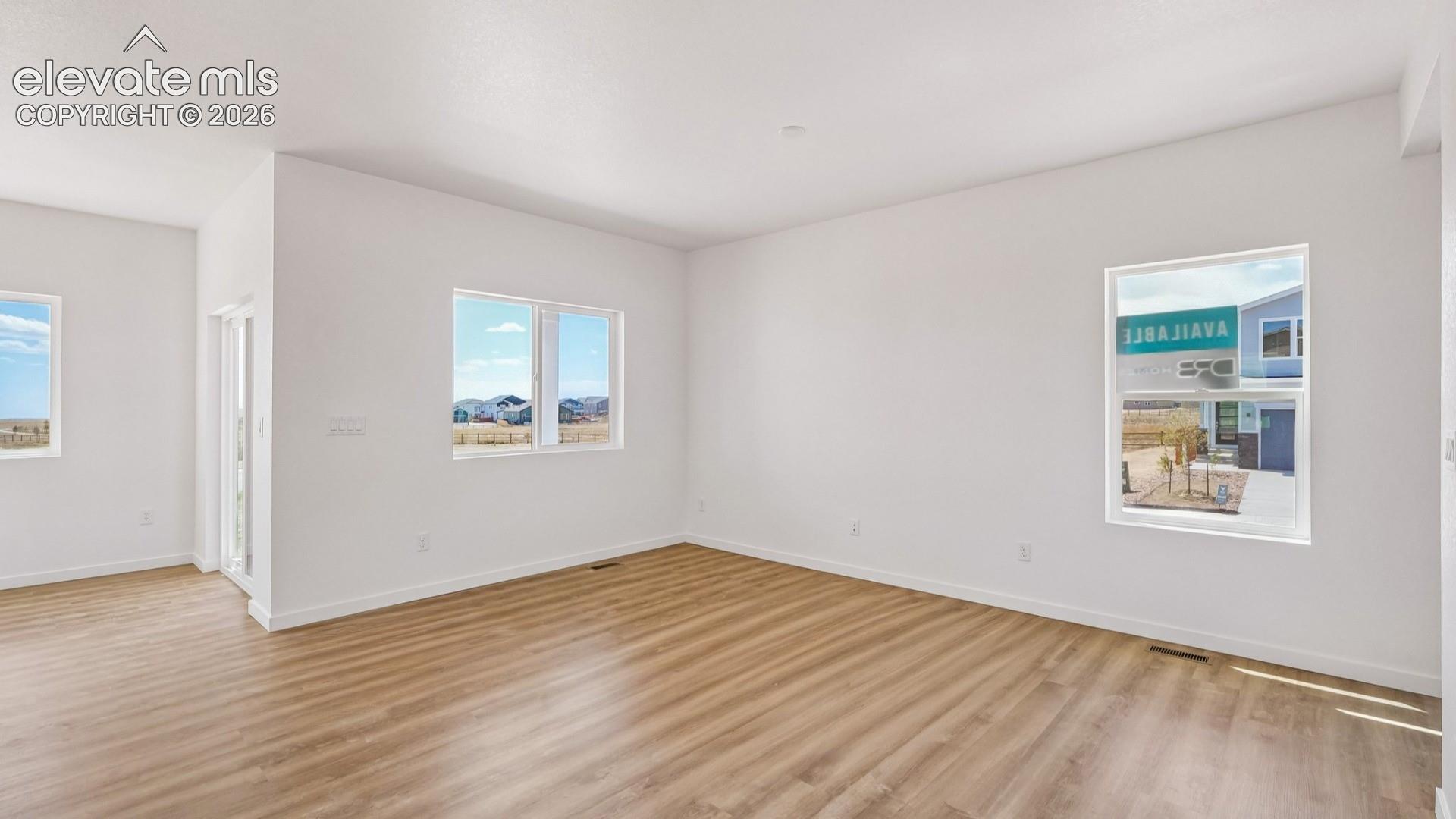 Open-concept interior featuring light wood-finish flooring, crisp white walls, and multiple dual-pane windows