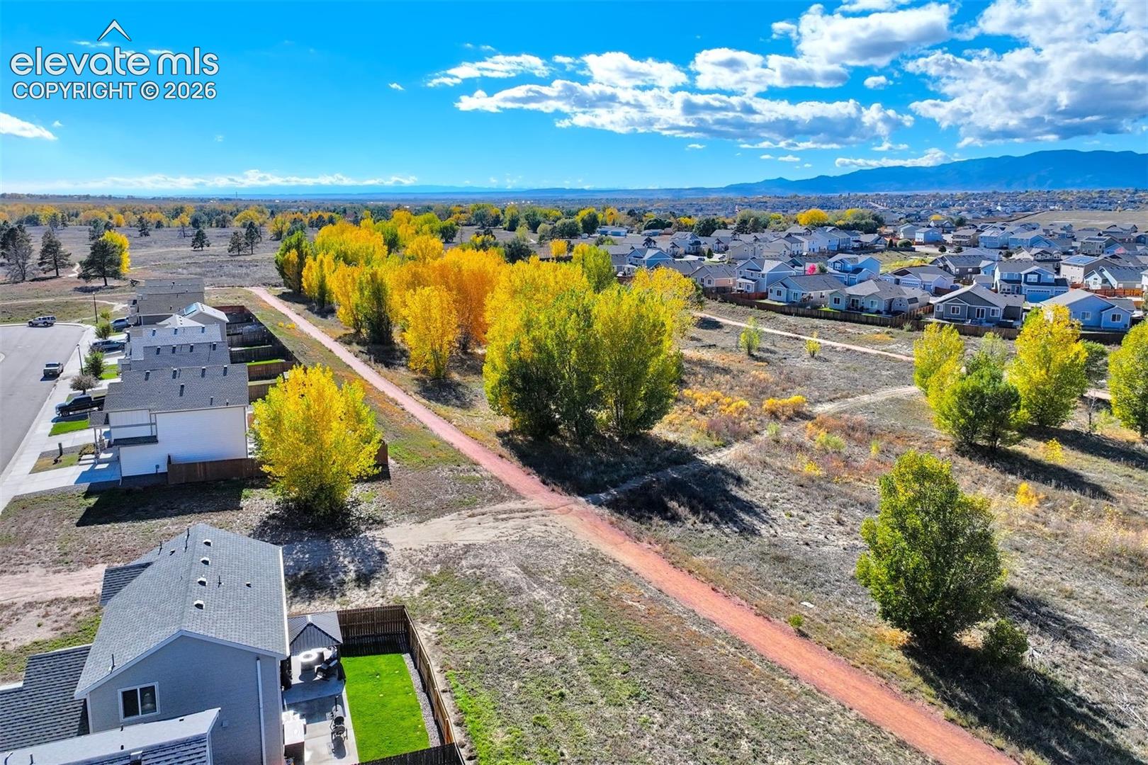 Aerial perspective of a multi-level residence featuring a gray composite shingle roof, a private fenced side yard, a concrete patio, and immediate proximity to a paved recreational trail