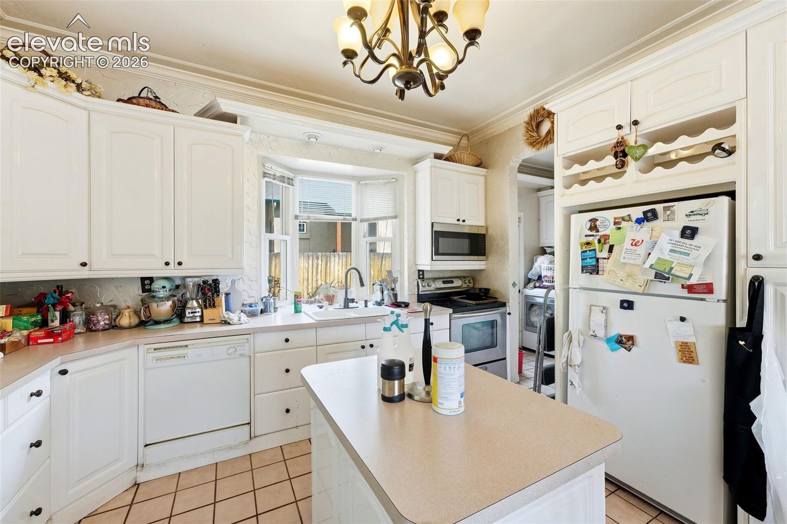 Kitchen featuring white cabinetry, a bay window, a central island, tile flooring, and integrated appliances