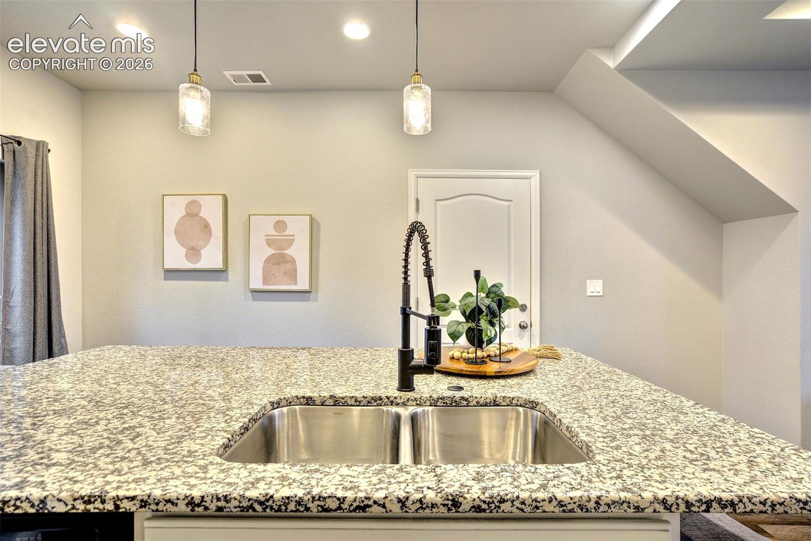 Kitchen island featuring a stone-composite countertop, stainless steel double-basin undermount sink, matte black gooseneck faucet, and two glass pendant lights