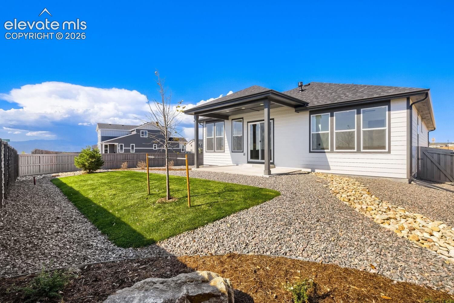 Expansive backyard featuring a manicured lawn, gravel pathways, and a covered patio with direct access to the interior