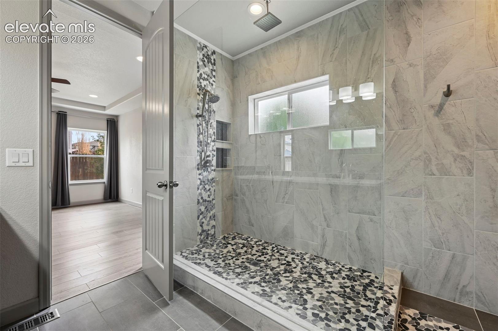 Walk-in shower featuring large-format tile surround, river stone floor, built-in dual recessed shelving, rainfall shower head, and a frameless glass enclosure