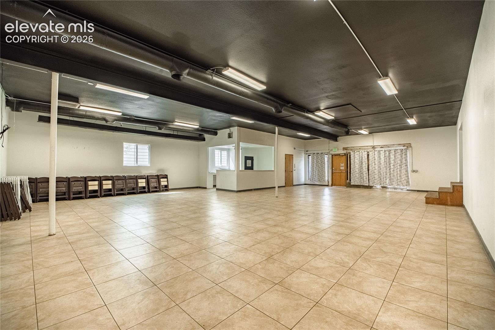Expansive open-concept space featuring ceramic tile flooring, a painted black ceiling, and multiple fluorescent lighting fixtures