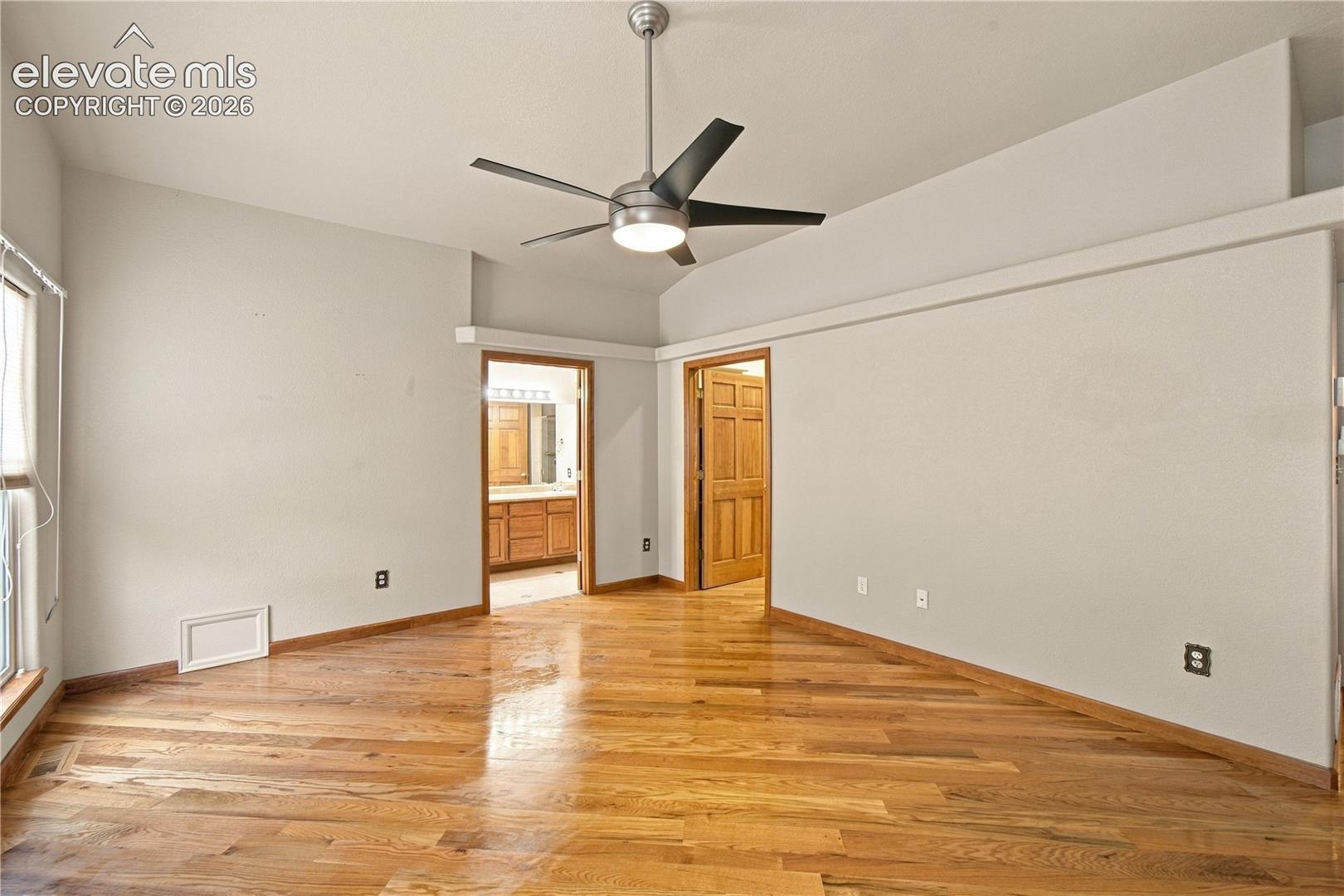 Room featuring wood-finish flooring, vaulted ceilings, and a brushed nickel ceiling fan with integrated lighting