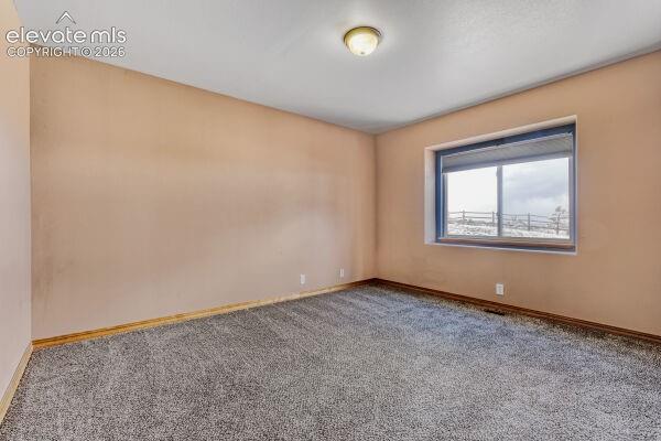 Spacious room featuring neutral-toned walls, grey carpet flooring, and a large window with a distant landscape