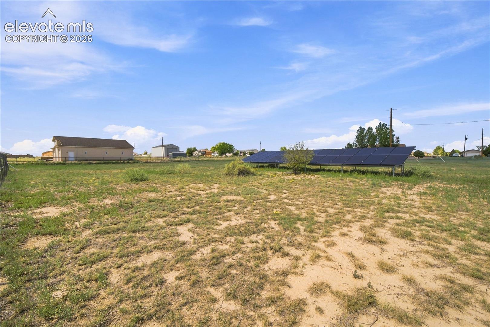 Expansive open land featuring solar panel arrays and a detached utility building with a roll-up door