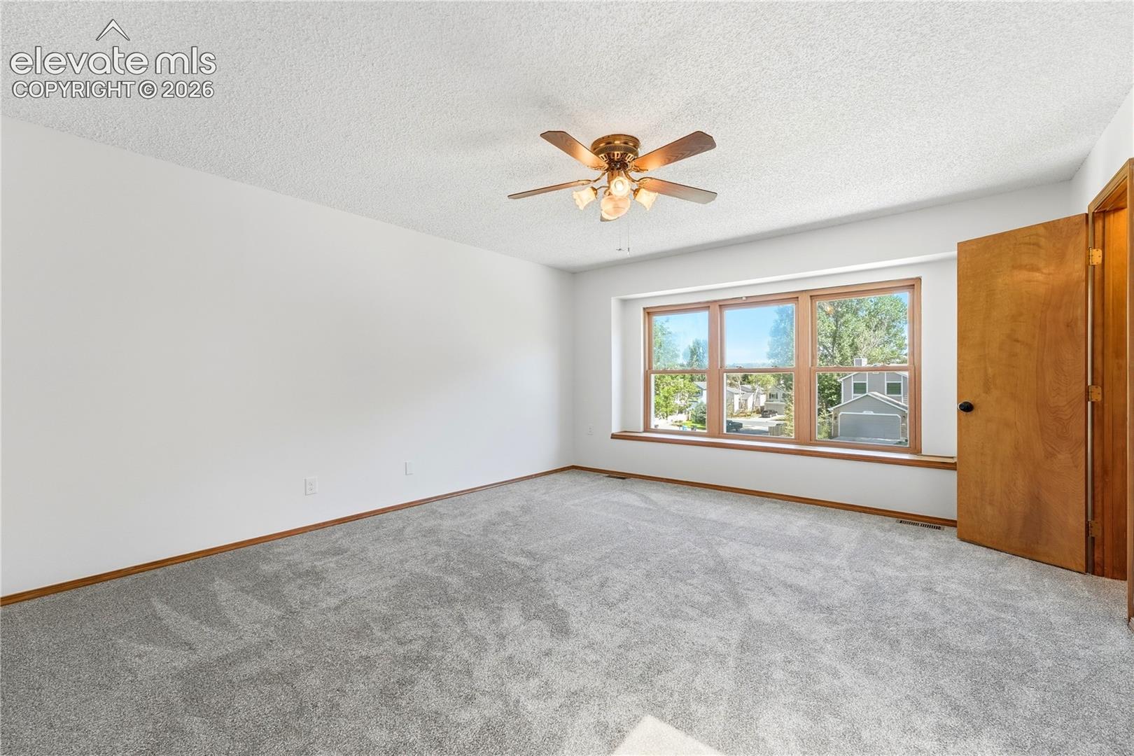 Spacious room featuring light gray carpeting, a wide window with faux wood vinyl trim, and a ceiling fan with lighting