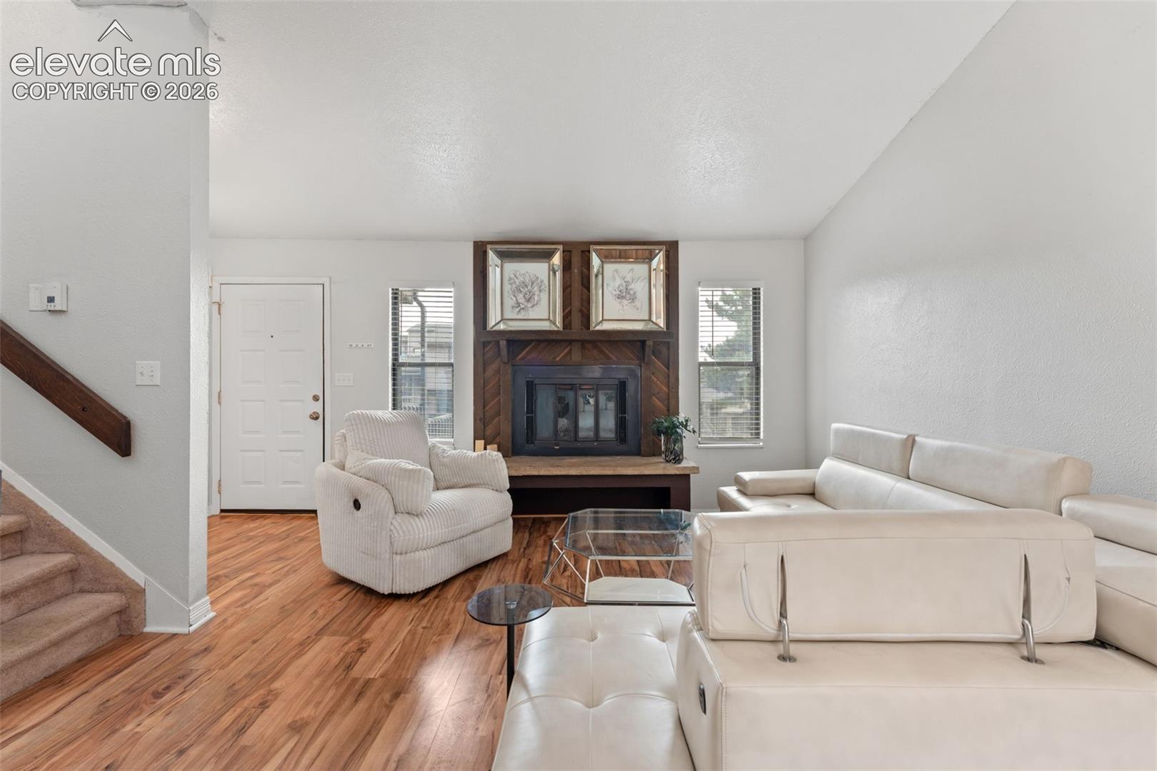 Wood-finish flooring throughout, a fireplace with a wood-paneled surround, and a white entry door with frosted glass