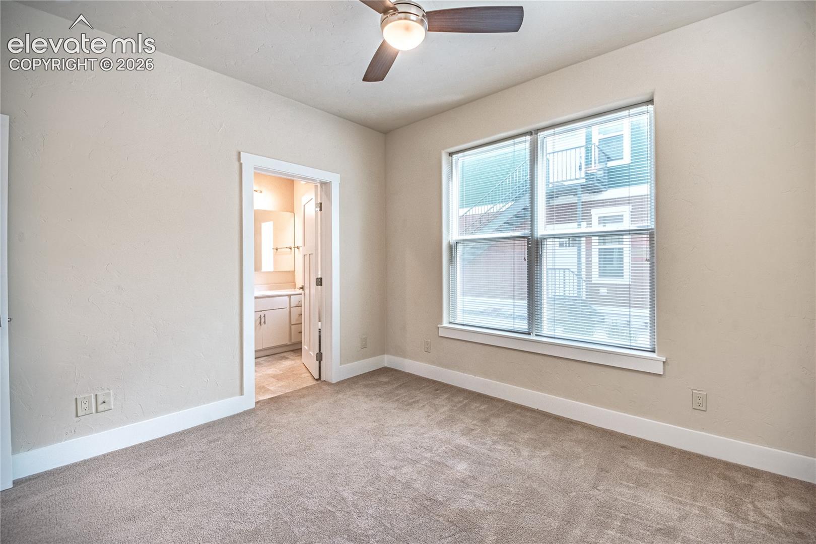 Carpeted room featuring a ceiling fan with light fixture, a large window with blinds, and white baseboards