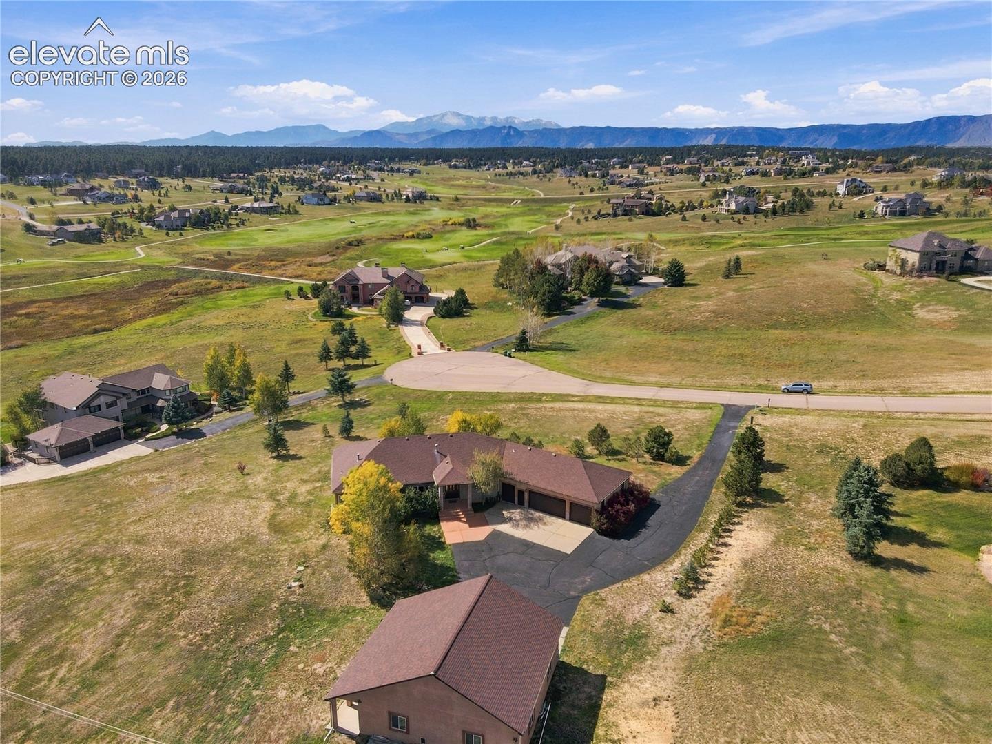 Mountain backdrop, expansive lot, paved driveway, mature trees, multi-car garage