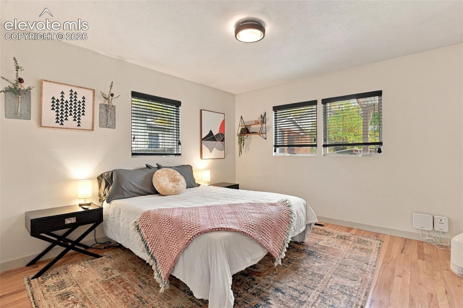 Wood-finish flooring, three double-pane windows with horizontal blinds, and a circular flush-mount ceiling light fixture